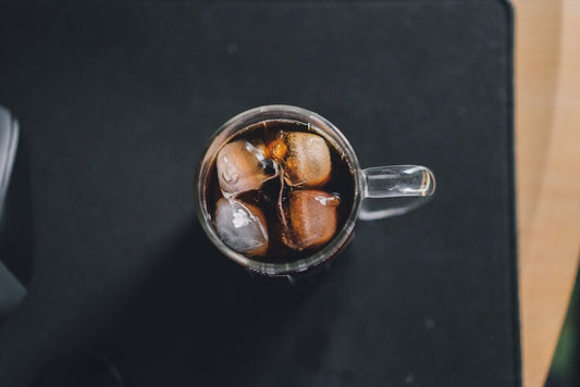 a glass filled with ice and coke on top of a table