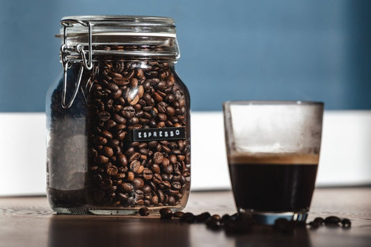 a glass of coffee next to a jar of coffee beans