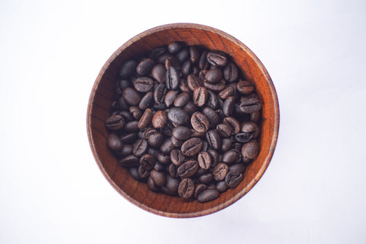 Coffee beans sit in a wooden bowl.