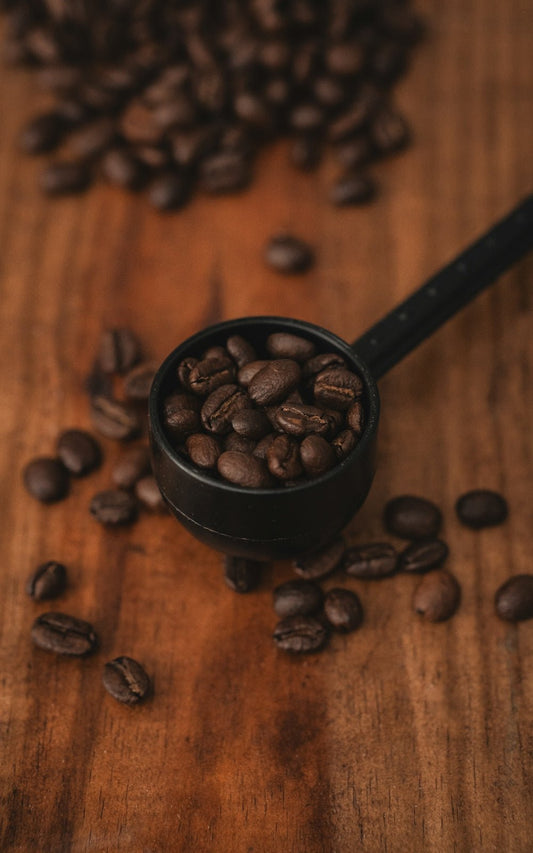 Coffee beans in a measuring scoop on wood.