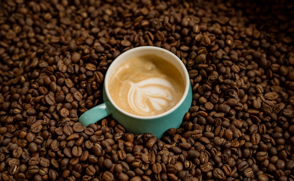 A coffee cup sits amidst roasted coffee beans.